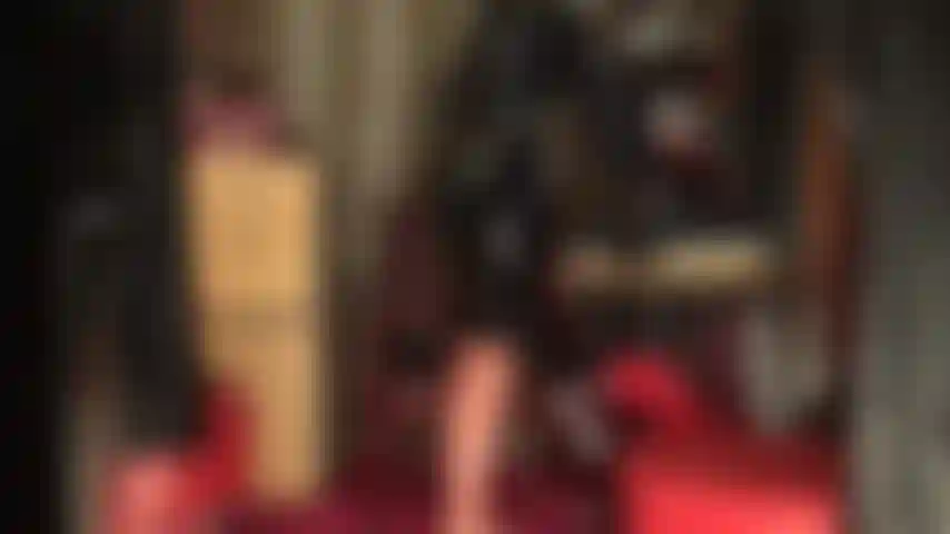 Roupa de borracha brilhante, meias e máscara - a deusa exibe suas curvas em látex justo, meias transparentes com costura e saia lápis preta com luvas. A roupa é completada com uma máscara de látex.