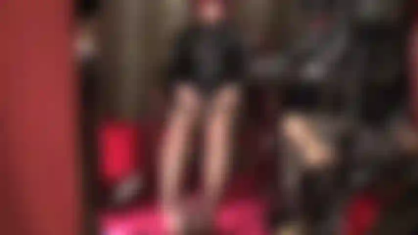 A senhora acaricia dois paus - vestida em pvc brilhante e meia-calça marrom, seus pés estão enrolados em um pau preto enquanto a senhora acaricia sua cinta-liga branca com as mãos nuas.