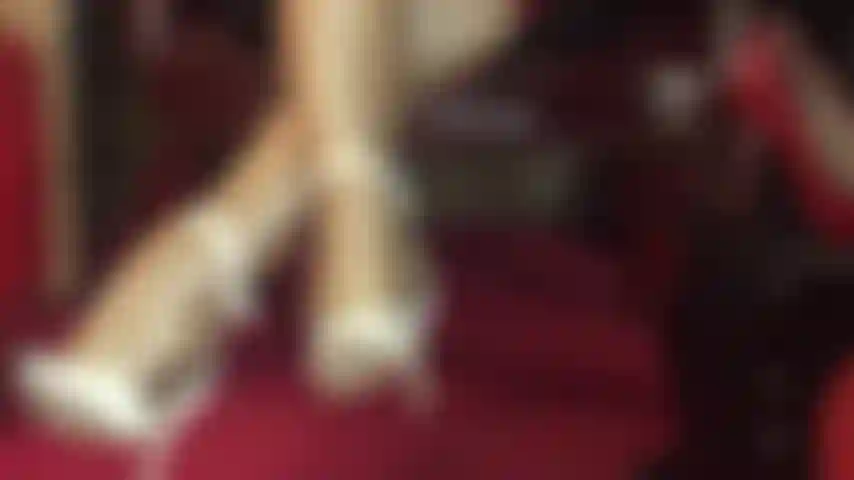 Com pernas de meia-calça incrivelmente brilhantes em camadas de náilon dourado e sandálias brancas de tira no tornozelo.