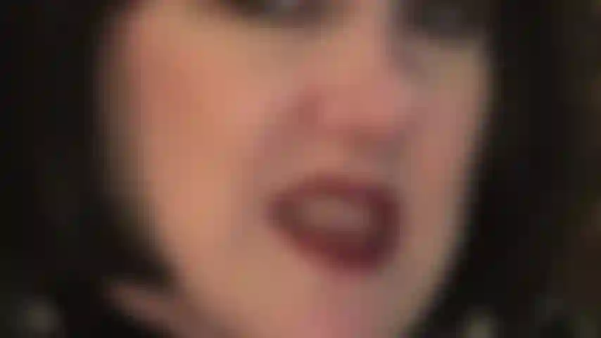 Com o rosto em close, usando uma peruca preta, provocando com lábios de batom vermelho e língua molhada, além de dentes e mãos enluvadas de couro que adorariam segurar suas bolas.