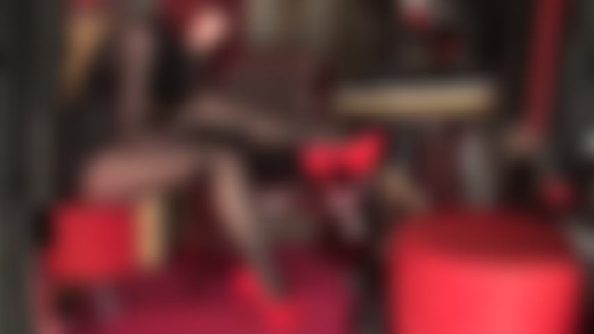 Provocando as pernas com meia-calça preta brilhante em camadas, couro e scarpins vermelhos. Pernas cruzadas, batom preto, saltos vermelhos vibrantes.