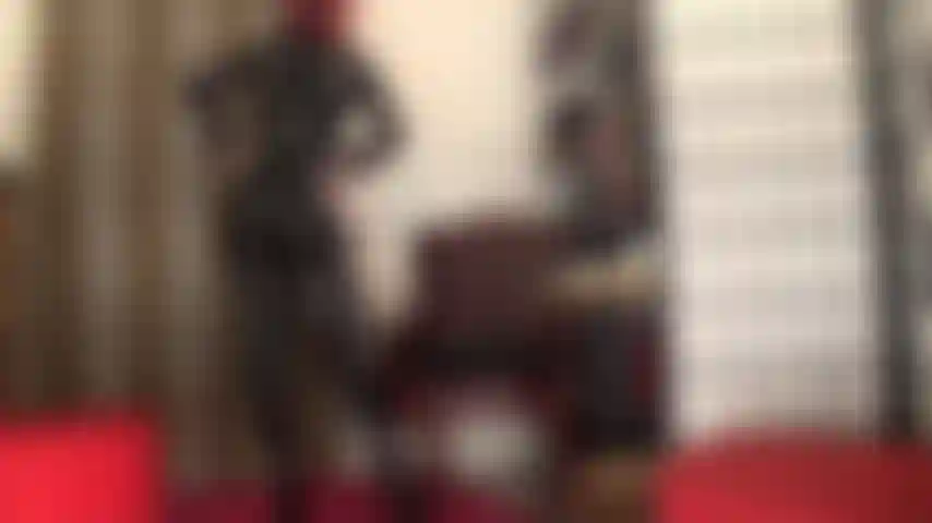 Com um macacão preto justo de pvc, espartilho e botas até a coxa.