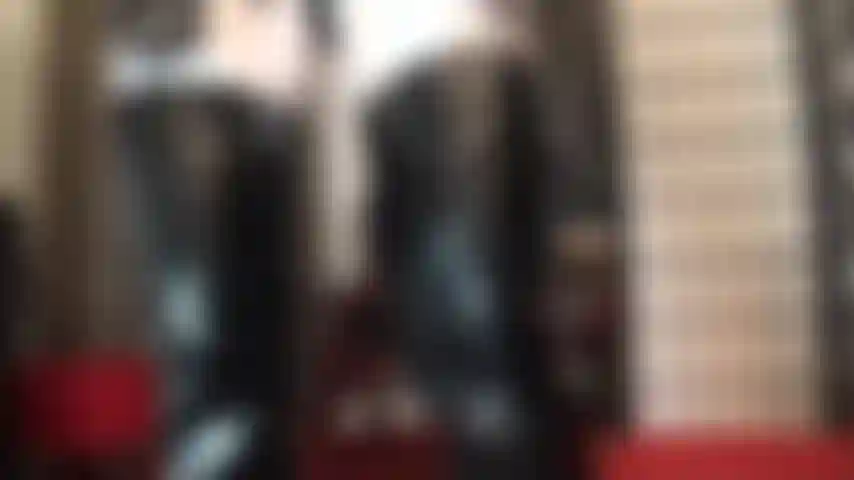 Com uma roupa preta e branca de botas e luvas de pvc brilhante combinadas com meia-calça de lycra branca brilhante.