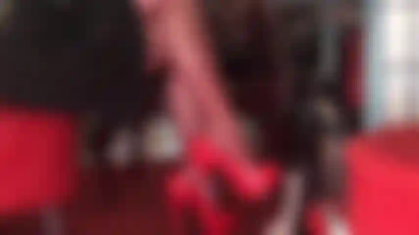 Pernas cruzadas sedutoras em meia-calça vermelha e sapatos vermelhos brilhantes provocam o pau dolorido do escravo.