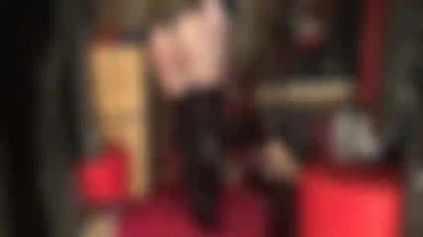 Uma deusa adoradora de bunda, com um body preto brilhante de pvc e botas de cano alto sobre meia-calça preta transparente.