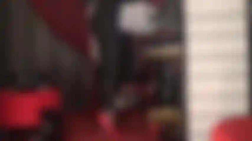 Com salto agulha vermelho e calcinha de renda vermelha em um macacão preto justo.