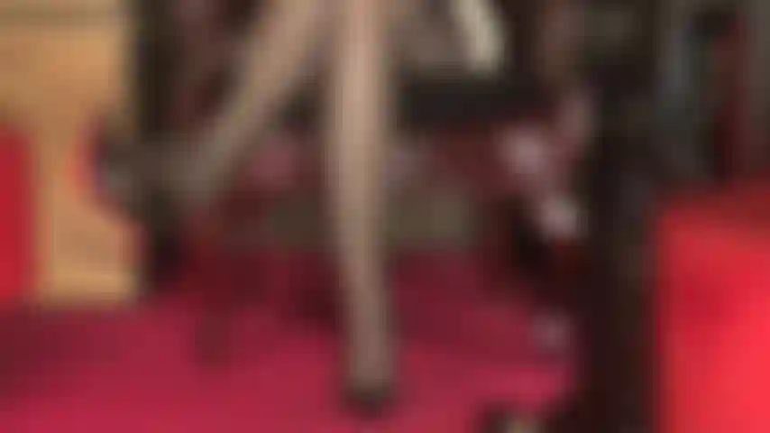 Uma visão sexy de pernas cobertas por meias, cinta-liga de várias tiras aparecendo, coxas cruzadas sensuais e dedos dos pés balançando um sapato de sola vermelha.