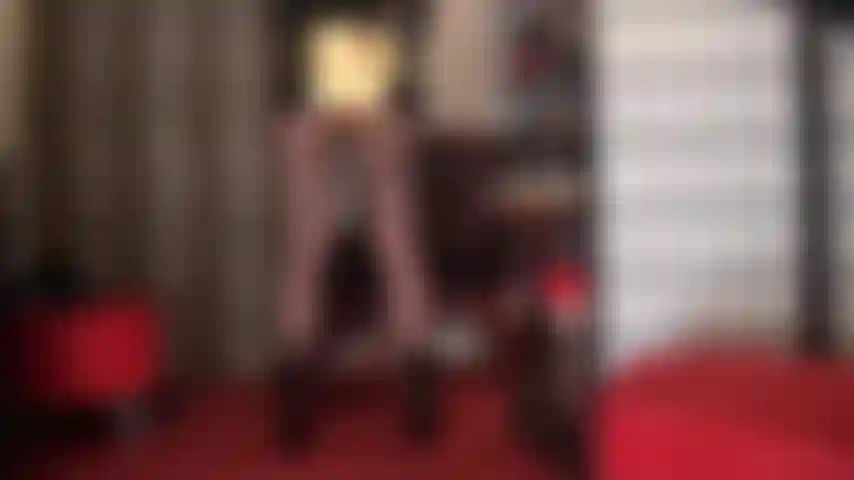 A mistress exibe sua bunda em shorts dourados metálicos brilhantes, suas pernas poderosas em meia-calça preta transparente, combinadas com botas pretas curtas de verniz.